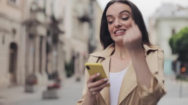 Jong aantrekkelijk meisje op zoek echt onder de indruk houden mobiele telefoon chatten en lachen maken ja gebaar staande op stad achtergrond close-up. — Stockvideo