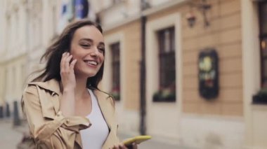 Kulaklık Takan Çekici Genç Kız Akıllı Telefonunu Kullanarak Müzik Dinliyor Memnun Görünüyor ve Şehir Arka Planında Yürüyor.