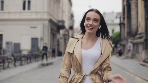 Portrét nádherné šťastné mladé dívky rozhovor s bezdrátovými Sluchátními telefony usmívající se chůze uvolněná na pozadí ulic City. — Stock video