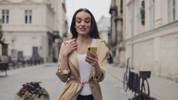 Preety Happy Young Girl vestindo fones de ouvido sem fio Fazendo uma chamada de vídeo Smiling Talking Walking Relaxed on the Street City Background Close Up . — Vídeo de Stock