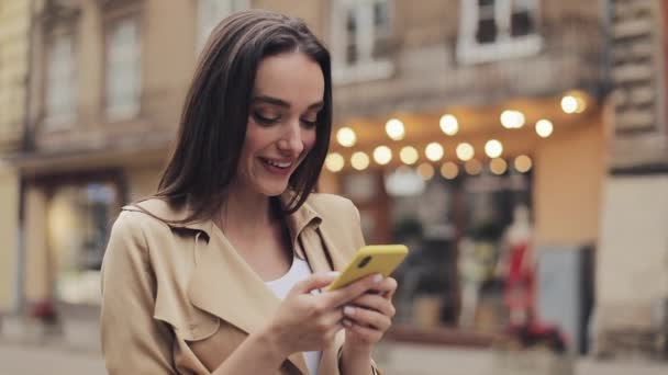 Jonge aantrekkelijke meisje houden mobiele telefoon chatten en lachen zeggen wow staande op stad achtergrond close-up. — Stockvideo