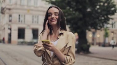 Kulaklık Takan Çekici Genç Kız Akıllı Telefonuna Müzik Dinliyor ve Şehir Arka Planında Gülümseyen Ayakta.