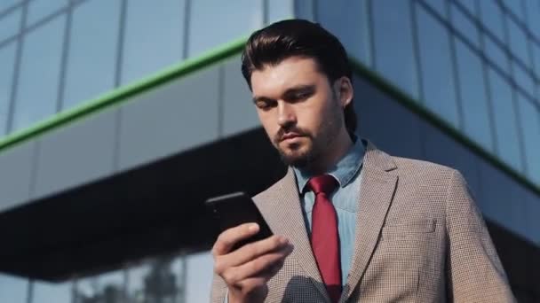 Empresario exitoso con traje elegante y reloj caro usando el teléfono caminando cerca de Bussiness Building Close Up — Vídeo de stock