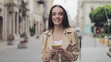Gülümseyen Güzel Genç Kız Portresi Cep Telefonu Tutan Kamera içine Loking ve Şehir Arka Planda Gülümseyen.