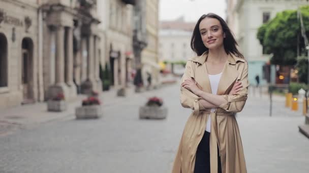 Porträtt av Happy fashionabla vacker ung flicka klädd i fashionabla Trench leende leende passage händer stående på stadens bakgrund. — Stockvideo