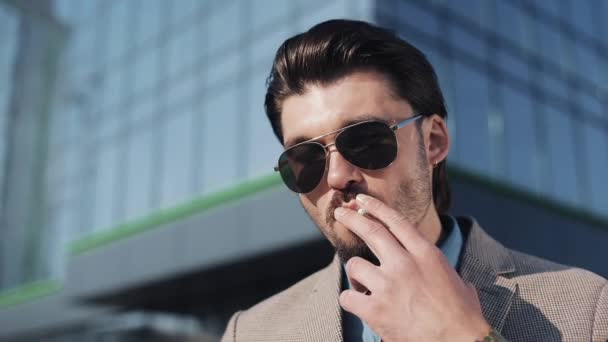 Hombre guapo en traje con corbata con gafas de sol Fumar cigarrillo en la calle cerca del edificio de oficinas — Vídeos de Stock