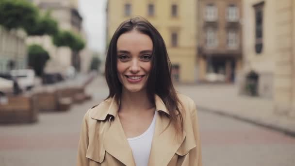 Portait de atractiva joven que lleva trinchera sonriendo y riendo de pie en el fondo de la ciudad de cerca. — Vídeos de Stock