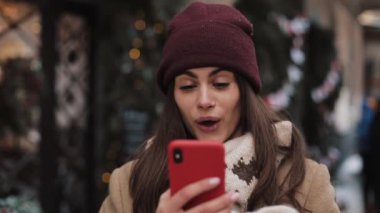 Close Up Kış Şapka ve Mittens Onun Smartphone kullanarak sohbet, Ekrana bakarak, Şaşırmış görünümlü ve Wow Standing Outdoor söyleyerek. İletişim, Tatil Konsepti.