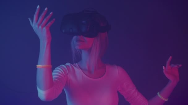 Happy Young Girl en realidad virtual juego de auriculares y las manos en movimiento en el aire de pie en la habitación con colores de iluminación de neón fondo futurítico. VR, concepto de nueva tecnología . — Vídeo de stock