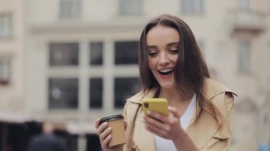 Genç Pretty Lady Looking Happy Drinking Coffe Gülümseyerek Akıllı Telefon Kullanarak Etkilendim City Street Close Up'ta Wow Yürüyüş Söyleyerek.
