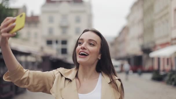 Schöne, glückliche junge Frau macht einen Videoanruf lächelnd plaudernd zu Fuß entspannt zeigt Stadt auf der Straße Hintergrund. — Stockvideo