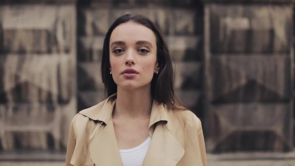 Kulaklık Giyen Ve Bej Açması Dik Duran Güzel Genç Kızın Portresi Başını Döndürüyor ve Yakın Çekimde Gülümsüyor. — Stok video