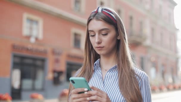 Giovane attraente ragazza capelli castani con fascia elegante indossando in camicia a righe numero di telefono su Smartphone e chiamando parlando e sorridendo in piedi sulla strada della città . — Video Stock