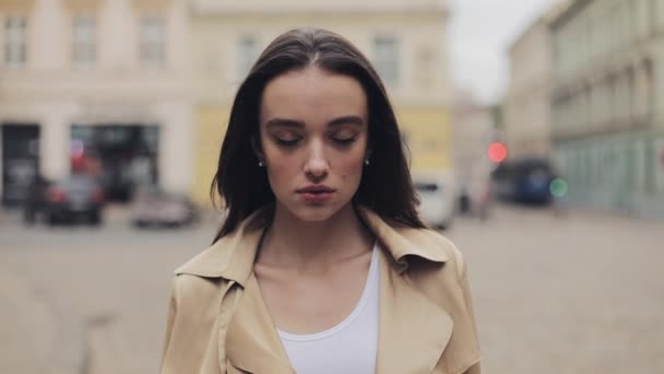Portret van vrij jong meisje zelfverzekerde ernstige meisje open ogen dragen beige loopgraaf staande in de rustige stad straat close-up. — Stockvideo