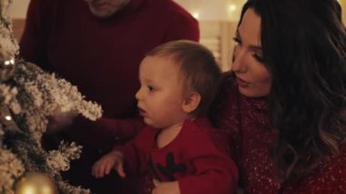 Mutlu Gülümseyen Aile Noel Ağacı yakınında Duran Küçük Bebek ve Rahat Oturma Odasında Dekorasyon Ağacı, Anne Zoom Bir Bebek Tutar, Aile Tatilleri Kavramı ve Yeni Yıl Close Up.