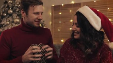 Lovely Çift Öpüşme Koca Close Up Aile Tatilleri ve Yeni Yıl Arka Plan Kavramı parlayan Işıklar ile Noel Ağacı yakınında Kanepede Oturan Mevcut Için Eşi Teşekkür.
