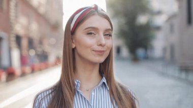 Çizgili Elbise ve Şık Headband Gülümseyen Kahverengi Saçlı ve Mavi Gözlü Genç Mutlu Kız Portre Close Up Şehir Caddesi'nde Ayakta Kamera arıyorsunuz.