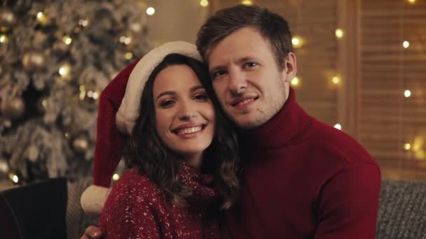 クリスマスツリー近くのリビングルームのソファに座って、休日と新年のカメラコンセプトを見つめながら、幸せな笑顔のカップルの肖像画. — ストック動画