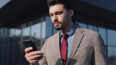 Yakışıklı İşadamı Takım Elbise Giyiyor ve Kravatlı Harika Görünüyor Telefonu kaydırıyor ve diyor ki İş Bulma Binası 'nın yanında Yürüyüş