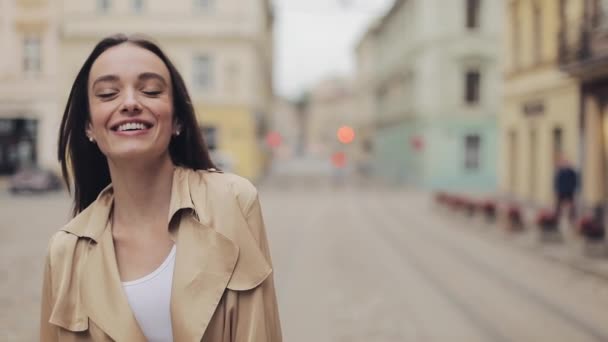 Porträtt av attraktiv ung vit flicka bär Beige skyttegrav leende och skrattande stående vid City bakgrund. — Stockvideo