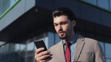 Çekici Genç İşadamı Şık Takımlar Giyiyor Cep telefonunu kullanıyor Şaşırmış ve tatmin olmuş görünüyor.