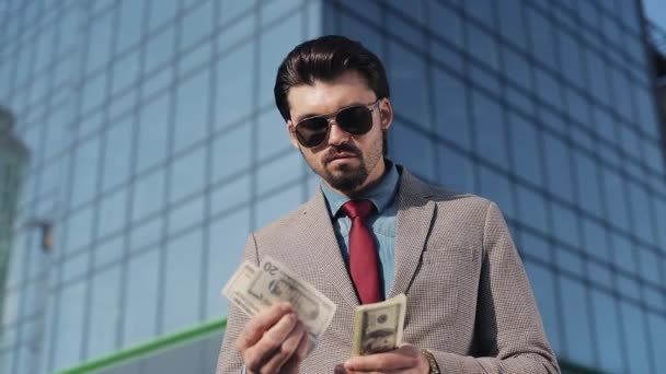 Bohatý mladý podnikatel v obleku nosí sluneční brýle počítání peněz v blízkosti mrakodrap — Stock video