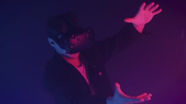 Sanal Gerçeklik Kulaklığı 'nda Genç Adam' ın Kapanışı, Hareketli Nesneler, Neon Işıklandırma Renkleri Fütüritik Arkaplan ile Odada Duruyor. Gelecek konsepti.