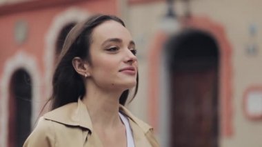 Gülümseyen, gülümseyen, gülümseyen, rahatlamış, eski şehrin arka planında yavaş çekim sol taraf görüntüsü olan güzel genç kızın portresi.
