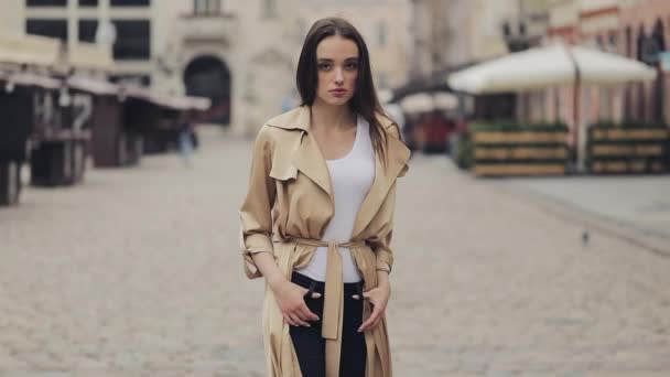 Retrato da atraente jovem senhora vestindo trincheira sozinha na rua da cidade com as mãos nos bolsos Olhando para a câmera com rosto sério . — Vídeo de Stock