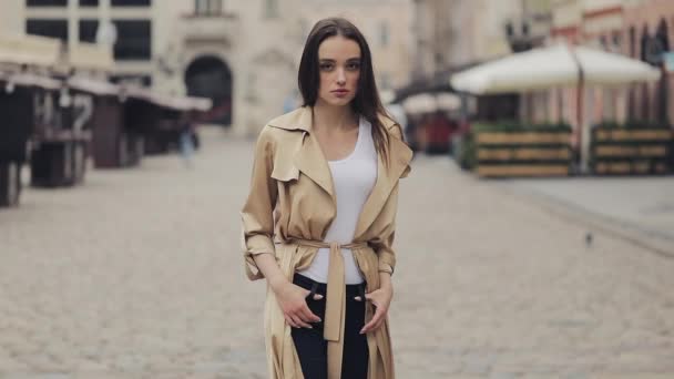 Portret van aantrekkelijke jonge dame dragen Trench Alleen staan in City Street met handen op zakken Kijken naar camera met ernstig gezicht. — Stockvideo