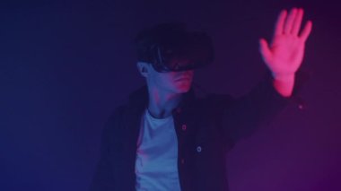 Sanal Gerçeklik Kulaklığı 'nda Genç Adam' ın Kapanışı, Oyun Oynaması, Bir şeye Dokunması, Neon Işıklandırma Renkleri Geleceğin Geçmişi ile Odada Durması. Gelecek konsepti.