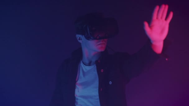 Nahaufnahme eines jungen Mannes in Virtual-Reality-Headset-Spiel, etwas zu berühren, steht im Raum mit Neonbeleuchtung Farben futuristischen Hintergrund. Zukunftskonzept. — Stockvideo