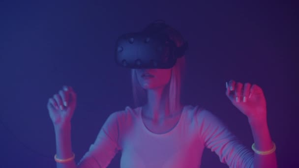 Кавказька дівчина, що носить віртуальну реальність, пересуває руки в повітрі, торкається віртуального екрану, стоїть на фоні неонового освітлення. — стокове відео