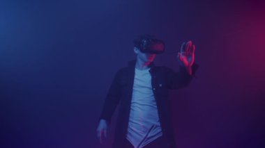 Yakışıklı Adam Sanal Gerçeklik Kulaklığı Giyiyor, Oyun Oynuyor, Hareketli Eller ve Hareketli Hareketler Yapıyor Fütürist Neon Işığı Arkaplanda Duruyor. Modern Teknoloji, Eğlence Konsepti.