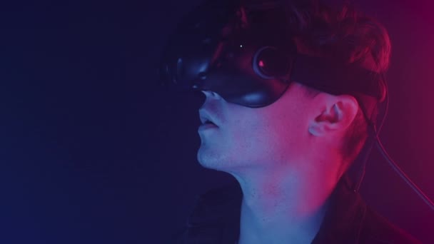 Porträtt av Thrilled Young Man bär Virtual Reality glasögon tittar upp och ler, säger Wow står i rummet med abstrakt neon belysning färger bakgrund. — Stockvideo