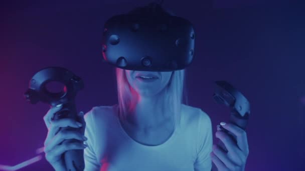 Молодая кавказская девушка в очках виртуальной реальности держит контроллеров, выглядящих испуганными и расстроенными, стоя на фоне футуристических неоновых огней. Виртуальная реальность, технологии. Закрыть . — стоковое видео