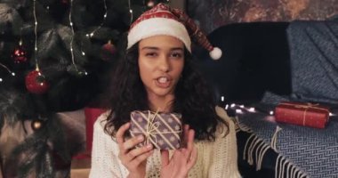 Noel Baba Şapkalı Çekici Genç Kız, Noel Ağacı 'nın yakınındaki Kameraya Hediye Kutuları' nı gösteren akıllı telefonunda görüntülü arama yapıyor. Yeni Yıl ve Noel Kutlama Kavramı.
