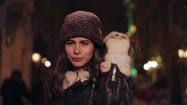Kış Şapkalı Mutlu Genç Kızın Yakın Portresi ve Akşam Işıkları Arkaplanda Düşen Kar Altında Yürüyen Eldivenler.