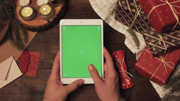 크리스마스에 나무로 장식된 탁자 위에 새로 만들어 진 하얀 태블릿이 있는 수직 녹색 화면에 손을 올리는 모습. — 비디오