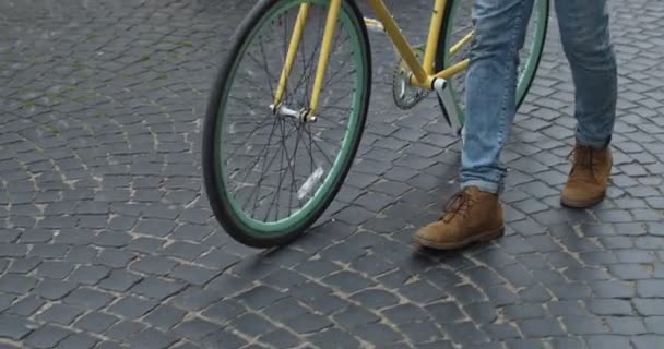 Nahaufnahme von Beinen in Jeans und lässigen Stiefeln, die auf dem alten Steinpflaster in der Nähe des modernen gelben dünnen Reifens laufen. Seitenansicht. — Stockvideo