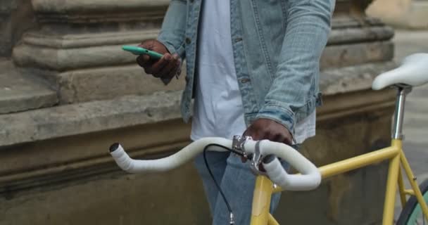Primer plano plano de bicicleta moderna amarilla con manillar blanco y mano de hombre afroamericano empujándolo en Old City Street . — Vídeo de stock
