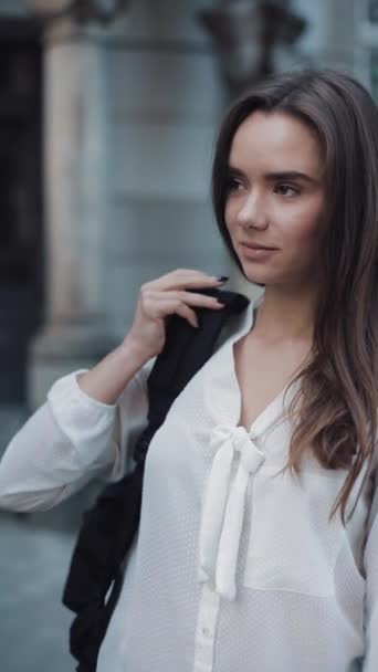 Close Up Shot of Pretty Brunette Student Girl Standing Outdoors while Putting a Bag on her Shoulder, Looking to Camera and Smiling. Vertical Video. — Stockvideo