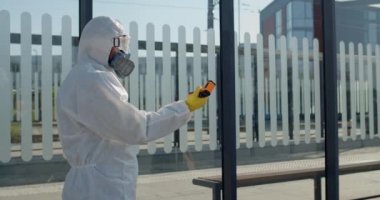 Koruyucu giysi ve maske takan bir tıp çalışanı, el kol hareketi yaparken tablet ve kadın yolcu taraması kullanıyor. Havaalanı yakınlarında sıcaklık kontrol noktası. Salgın ve koronavirüs kavramı.