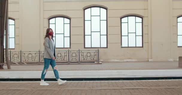 Widok z boku tysiąclecia brunetka dziewczyna w casual ubrania spaceru na pustej stacji kolejowej platformy. Młoda, modna kobieta w ręcznie robionej masce. Koncepcja pandemii wirusa. — Wideo stockowe