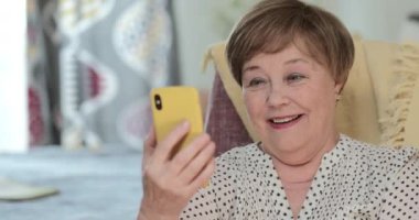Happy old woman having video conversation with family member and smiling. Cheerful elderly lady talking while using frontal camera of her smartphone. Concept of communication.