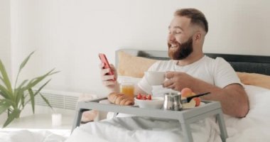 Sakallı adam kahve fincanı tutuyor ve yatakta yatarken komik mesajlar ya da şakalar okuyor. 30 'lu yaşlarda gülümseyen bir adam kahvaltı yaparken akıllı telefon ekranına bakıp gülüyor..