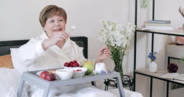 Olgun, güzel bir bayanın bacaklarında Trey 'le oturduğu ve sabahları eğlendiği ön manzara. Yatakta kahvaltı ederken çiçek kokusu alan yaşlı bir kadın. Boş zaman kavramı ve rahatlama.