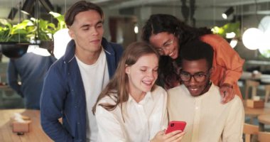 Bir grup neşeli insan akıllı telefon ekranına bakarken gülüyor. Mutlu arkadaşlar, rahat bir restoranda birlikte vakit geçirirken fotoğraflara bakarlar. Olumlu duygular kavramı.