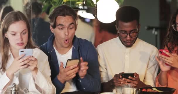 अपने दोस्तों को स्मार्टफ़ोन सामग्री दिखाने और मुस्कुराते हुए एक युवा आदमी का दृश्य बंद करें। कैफे में बैठे हुए अपने फोन का उपयोग करते हुए खुशहाल मिलेनियल लोग एक साथ समय बिताते हुए . — स्टॉक वीडियो