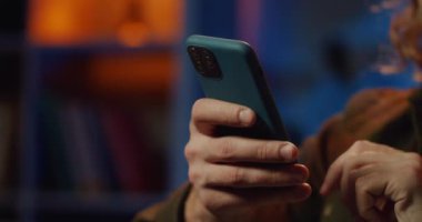 Akıllı telefonu tutarken erkeklerin elleri ekranı sarıyor ve dokunuyor. Genç adam internete girmek için telefon kullanıyor. İletişim ve eğlence anlayışı. Ev geçmişi..